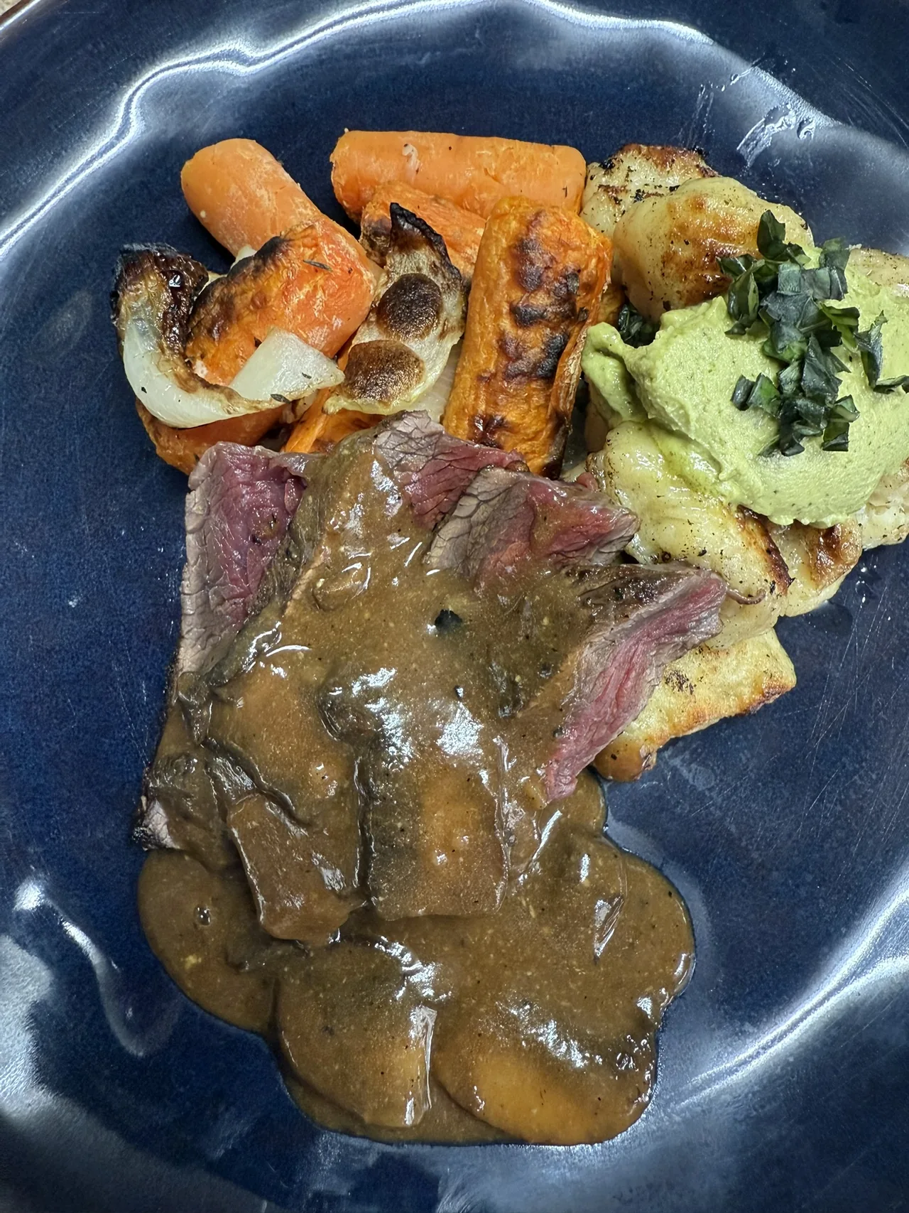 Grilled elk tenderloin with sauce, roasted carrots, and gnocchi on a dark blue plate
